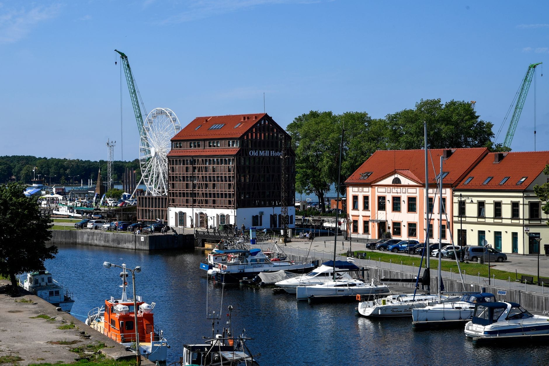 Beautiful view of Klaipėda's waterfront featuring Old Mill Hotel, yachts, and a Ferris wheel on a sunny day.