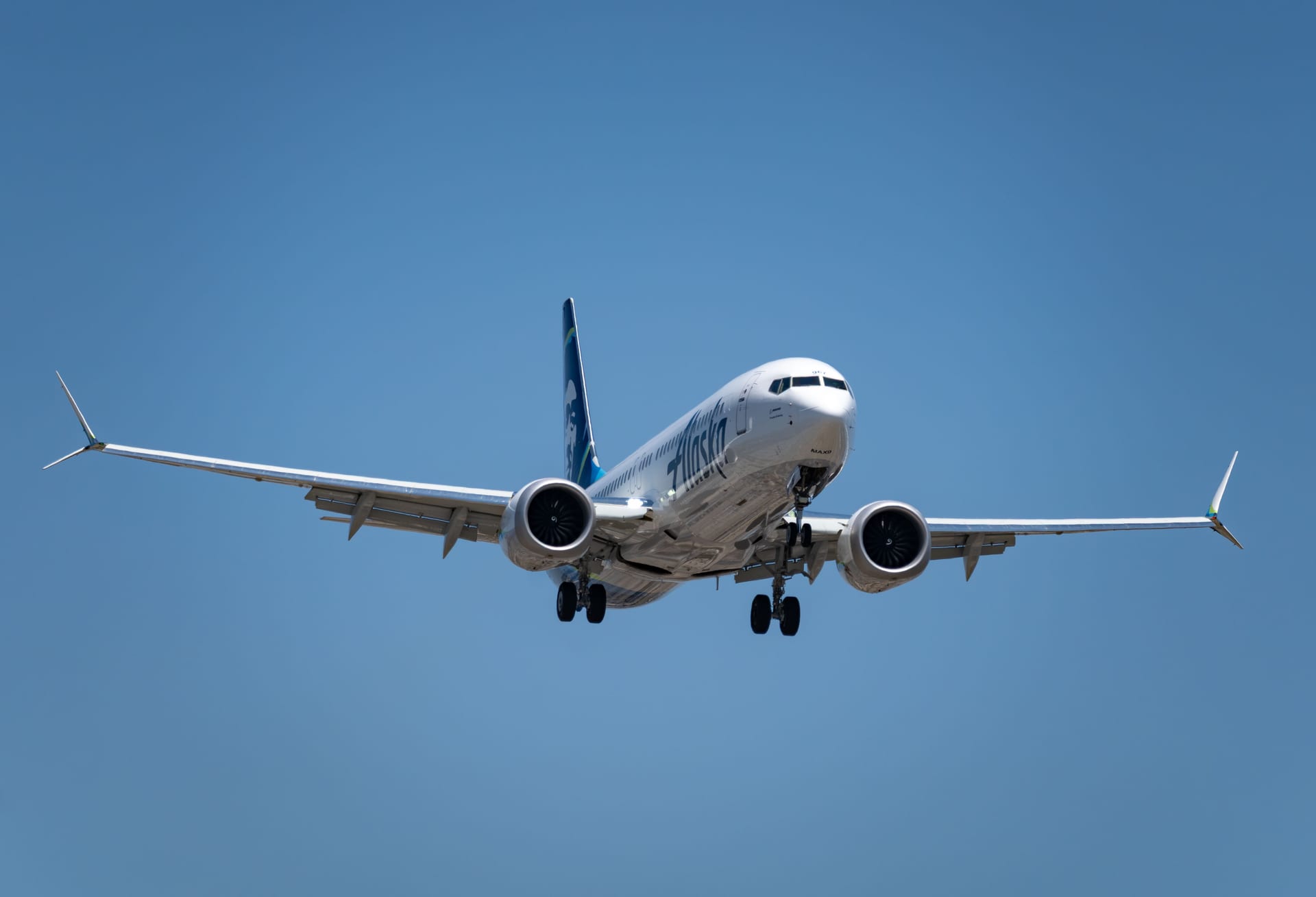 Commercial airliner captured mid-flight with landing gear down against a clear blue sky.